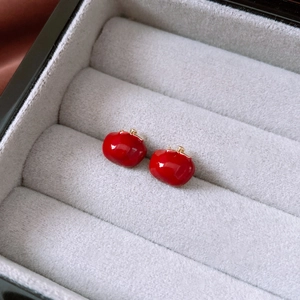 Macro shot of red apple-shaped stud earrings with gold leaves on gray velvet
