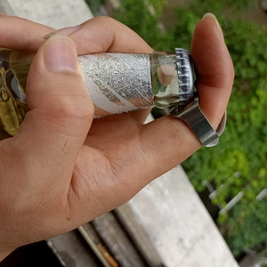 Close-up of a stainless steel bottle opener ring being used to open a glass bottle cap