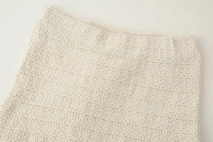 Gros plan détaillé du tissu en maille beige montrant la texture côtelée et l'ourlet doux