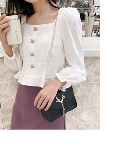 Close-up of black crossbody bag with golden deer head buckle and tassel on white top