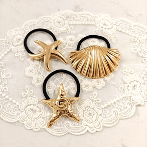 Three-piece gold starfish and seashell stainless steel hair ties on white lace background