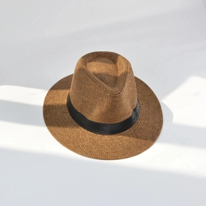 Détail d'un chapeau Panama en paille marron avec ruban gros-grain noir sur fond blanc