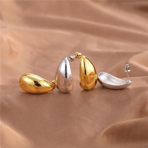 Minimalist metallic teardrop earrings in polished gold and silver on textured fabric