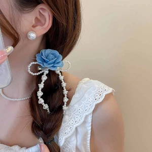 Detail of fabric flower hair clip with pearl bow and tassel worn by a model