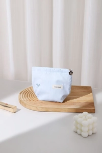 Détail d'une trousse à maquillage rayée bleu clair avec broderie nœud et fleur sur zip