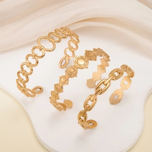 Dettaglio di tre bracciali rigidi in acciaio inossidabile dorato con maglie e dischi