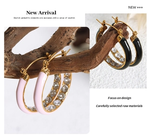 Detail of pink and black enamel gold earrings with sparkling crystals on wooden branch