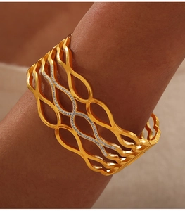 Detailed close-up of golden hollow wave bangle with sparkling white rhinestones on wrist