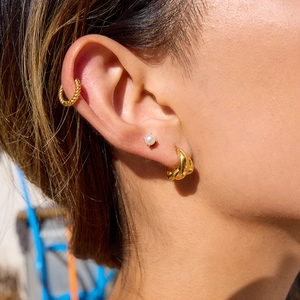 Close-up of model wearing 18K gold plated triple layered twisted hoop earrings and pearls
