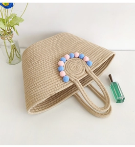 Detail of beige straw tote bag with colorful pom poms and handmade woven handles