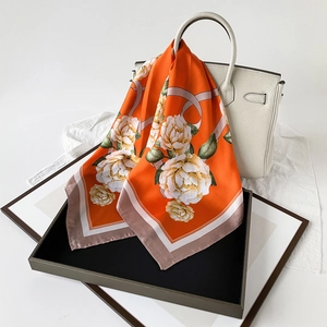Floral satin silk scarf draped over a white leather bag featuring orange peony prints