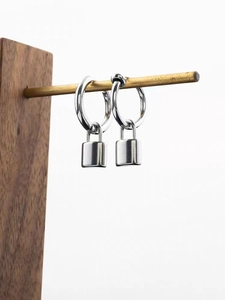 Polished silver lock pendant hoop earrings displayed on a minimalist wooden stand