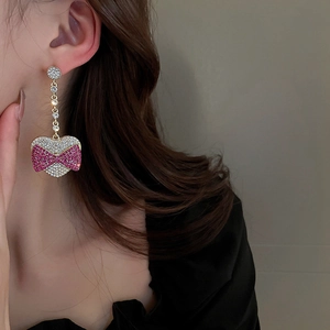 Detail of long gold heart earring with pink rhinestone bow worn by a model