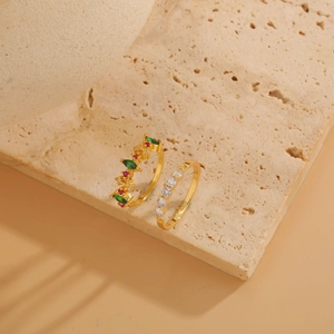 Detail of 14K gold plated geometric rings with green and red zircons on beige stone