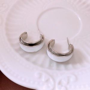 Macro detail of silver C-shaped earrings with white enamel on a white ceramic plate