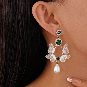 Detail of silver butterfly earrings with green stones and white teardrop pearls on a model