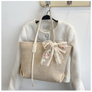 Detail of cream straw tote bag featuring delicate 3D lace embroidery bow on the front