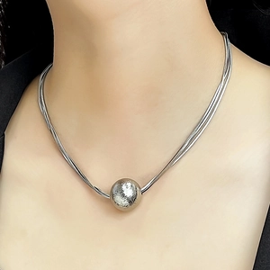 Close-up of a silver multilayer snake chain necklace with a textured ball pendant