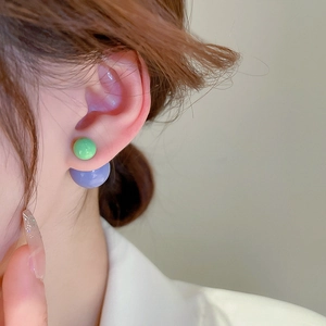 Close-up of minimalist green and lilac dual-ball stud earrings worn on the ear