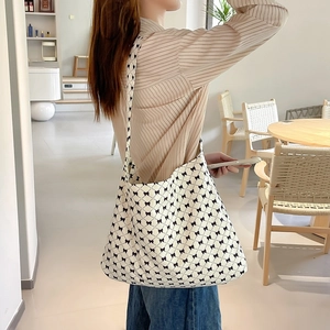 Detail of canvas tote bag with black bow print worn by a model in a cozy cafe setting
