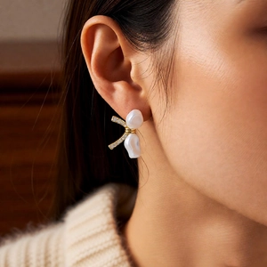 Close-up of 18k gold plated bow earrings with pearls on model ear in soft light