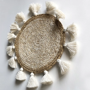 Dettaglio di decorazione murale boho in paglia intrecciata con nappe bianche e trama a spirale