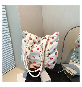Close-up of white corduroy tote bag with red strawberry pattern and long handle straps