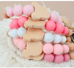 Close-up of silicone and wood baby pacifier clips with pink beads on a woven macrame rug