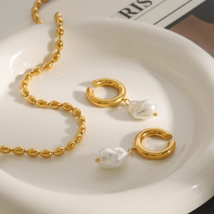 Gros plan de boucles d'oreilles en C dorées avec perles baroques sur plat céramique