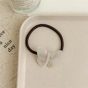 Detail of iridescent white acetate butterfly hair tie on a decorative beige tray
