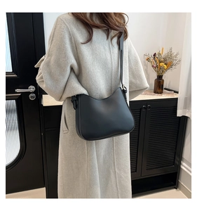 Model wearing a black crescent-shaped leather shoulder bag over a light-colored coat