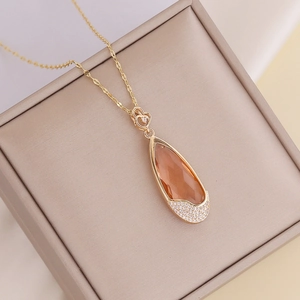Elegant gold necklace with teardrop orange stone and zircon pendant on a gift box