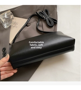 Detail view of a black rectangle handbag with fine leather texture on a grey blazer suit