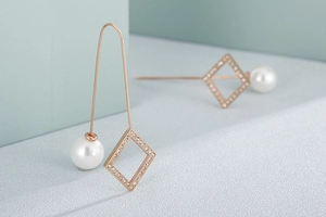 Detail of rose gold clover earrings with rhinestones, long ear wires, and white pearls