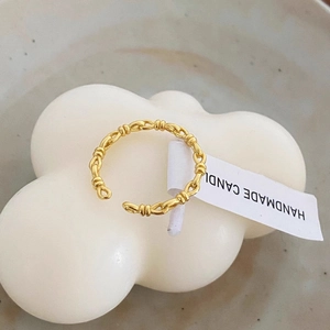 Detail view of a gold knot woven ring on a white decorative candle backdrop