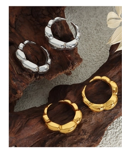 Artistic close-up of chunky gold and silver bamboo style earrings on rustic wood stand