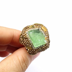 Macro shot of vintage gold ring featuring a raw green stone and pavé crystal details