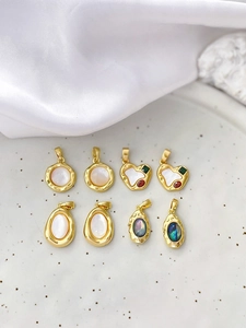 Detail of 18k gold-plated heart and oval charms with natural shell inlays on ceramic