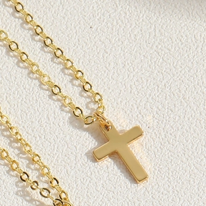 Close-up of a polished gold cross pendant necklace with a delicate chain on white background