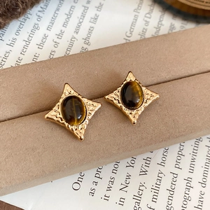 Detailed macro view of retro star-shaped earrings with oval tiger eye stone and gold base