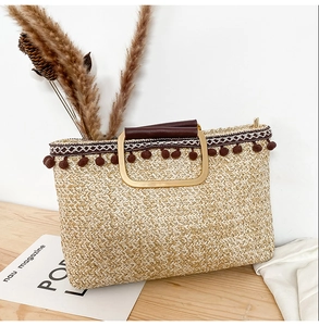 Detail of hand-woven straw tote with brown tassel charms and golden D-shaped handles