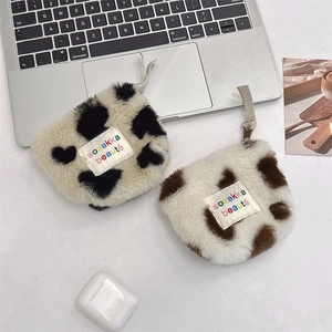 Flat lay of plush cow print coin purses for earphones and lipstick on a white desk