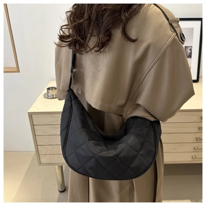 Chic black quilted nylon crescent bag worn over a trench coat for a stylish urban look