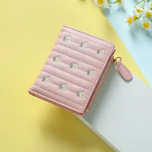 Quilted light pink mini wallet with daisy embroidery and secure zip closure on a platform