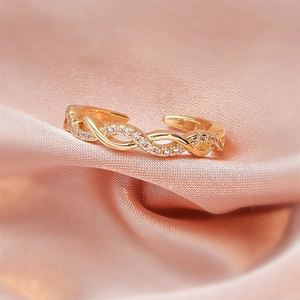 Macro detail of adjustable golden orbital ring with sparkling zircon inlays on pink silk