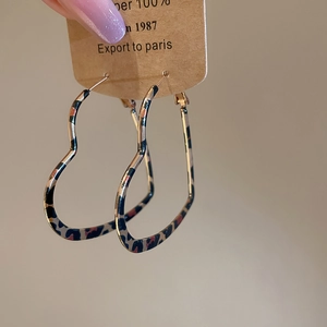 Macro view of leopard print heart earrings being held against a warm background