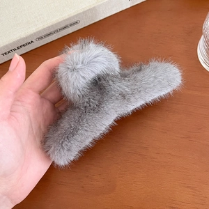 Détail d'une grande pince à cheveux grise en fausse fourrure tenue sur fond en bois