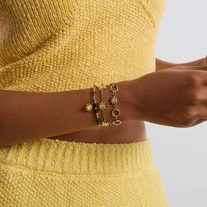 Close-up of stacked gold sun charm bracelets with colored beads on woman's wrist