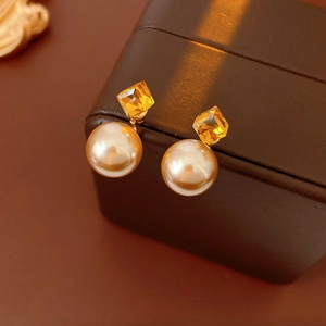 Detail of vintage gold pearl earrings with amber gemstone on a brown leather jewelry box