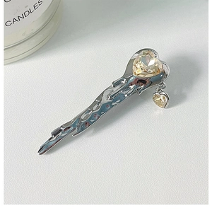 Macro view of liquid metal hair clip featuring amber heart crystal and pendant detail